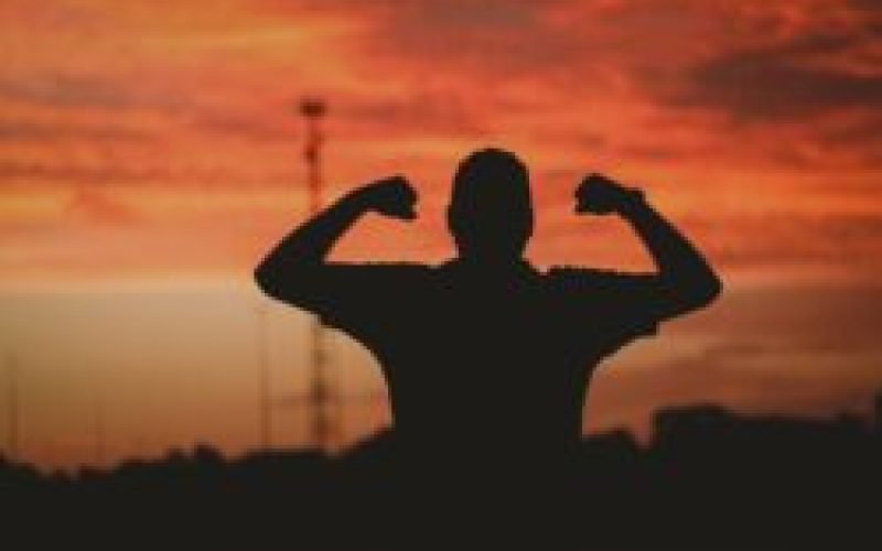 A silhouette of a strong man under a cloudy sky during the golden sunset